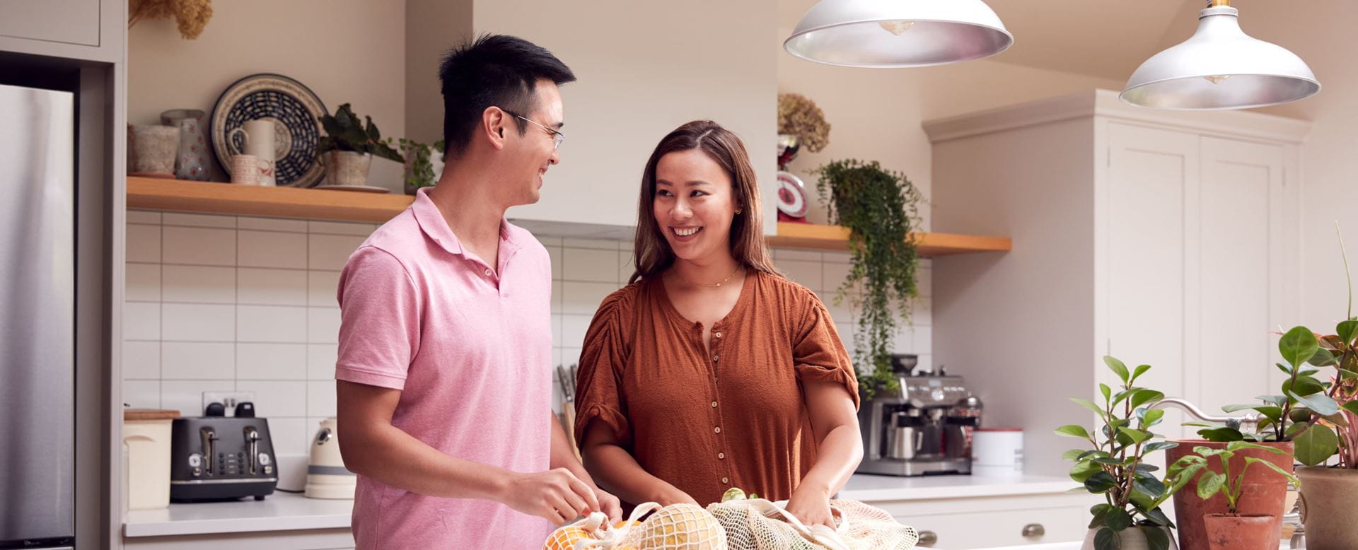 A man wearing a pink polo and a woman in an orange shirt standing in the kitchen