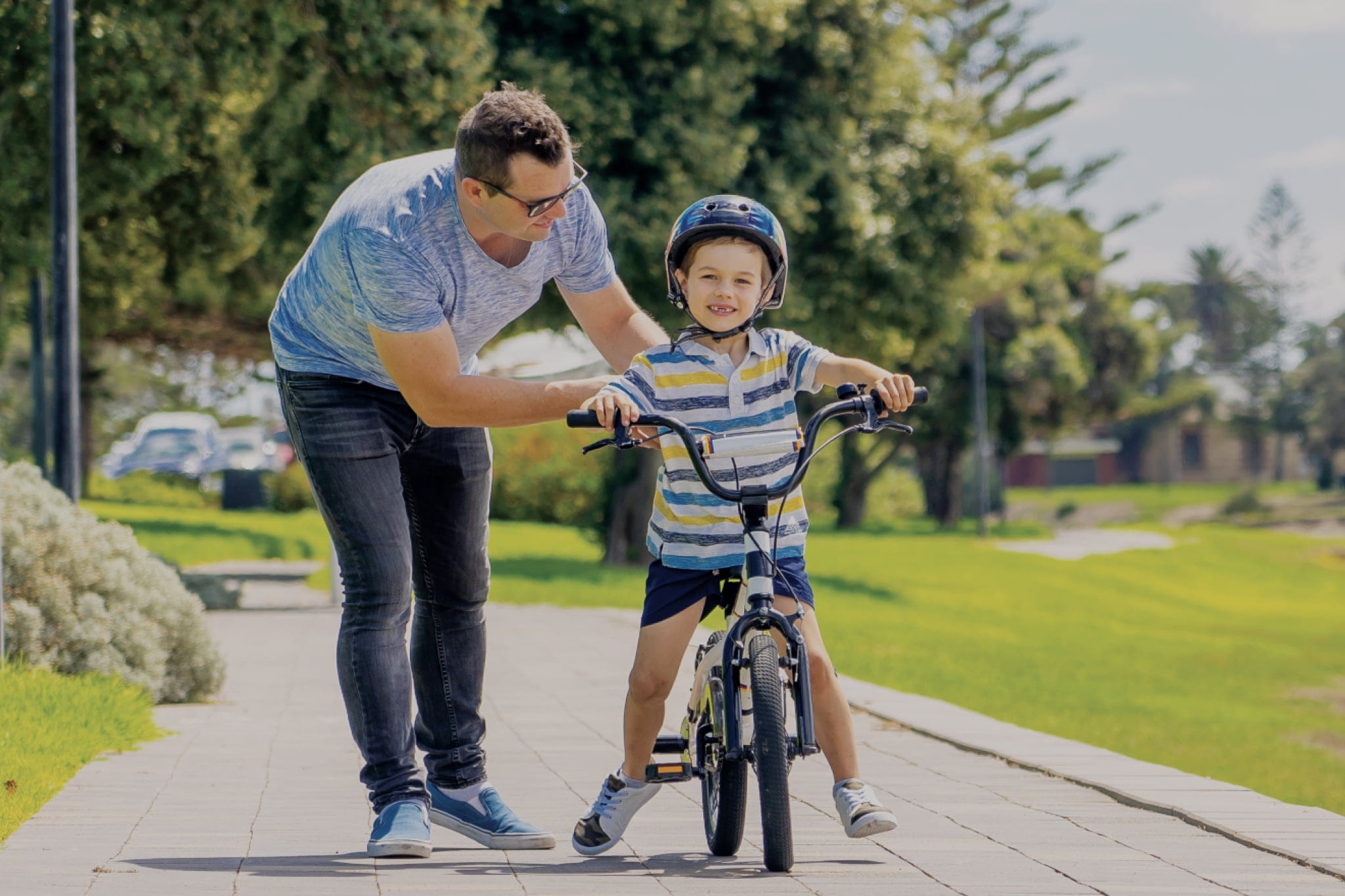 A young boy riding a bicycle in a local park with his dad supporting him