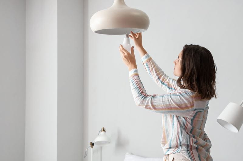 A woman adjusting a light fixture inside her home
