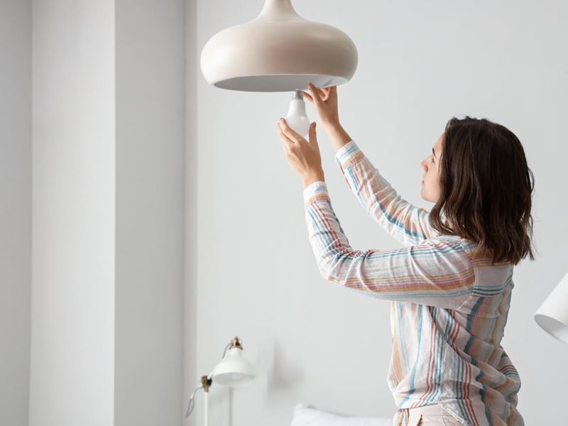 A woman wearing a striped shirt replacing a light bulb in her study.
