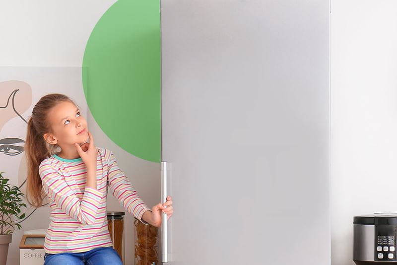 A little girl sitting on a chair in front of a refrigerator