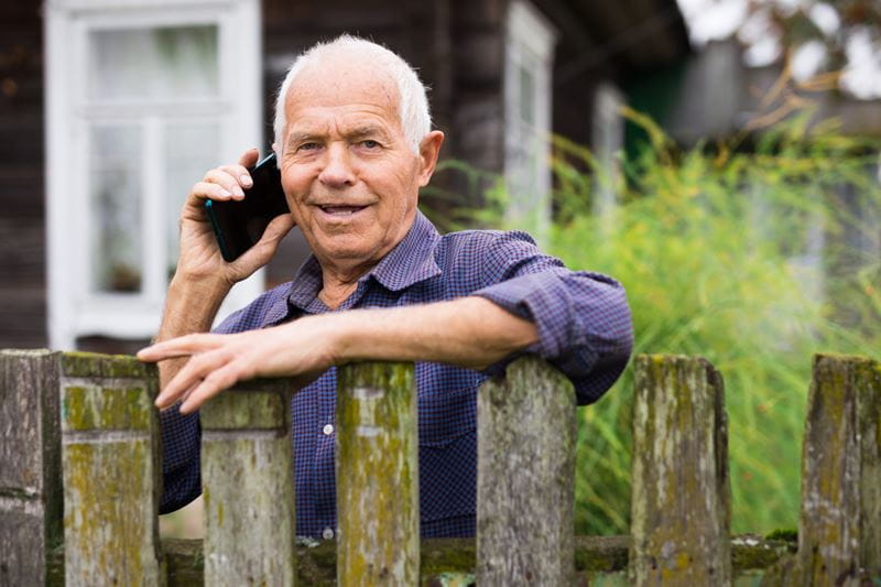 Older man leaning on a fence talking on a mobile phone