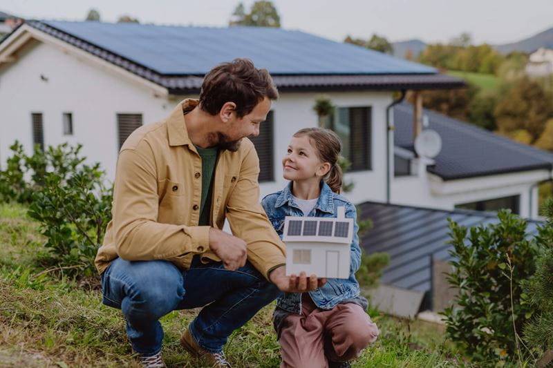 Father and daughter smiling and crouching in front of their house with solar