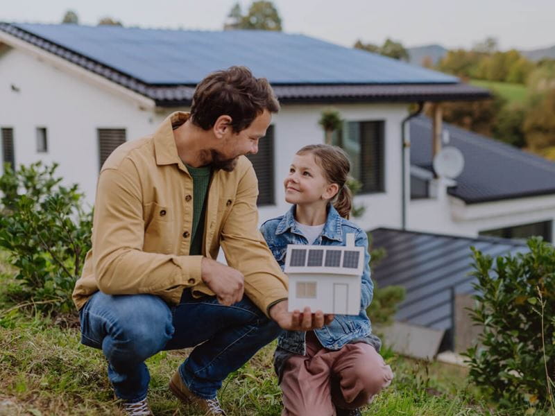 Father and daughter holding a solar house model smiling at each other
