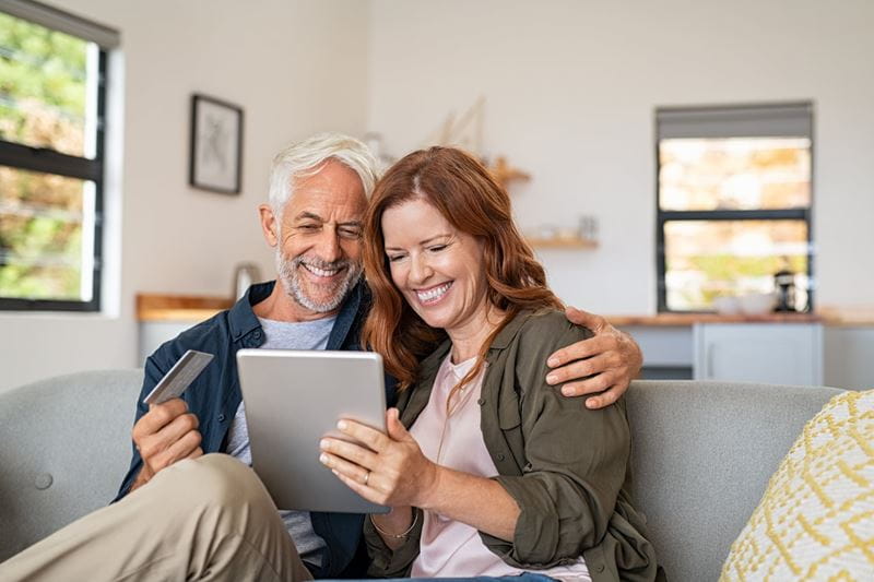Smiling couple sitting on the lounge using a tablet in living room