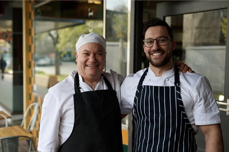 Two local restauranteurs standing side-by-side with their arms around each other