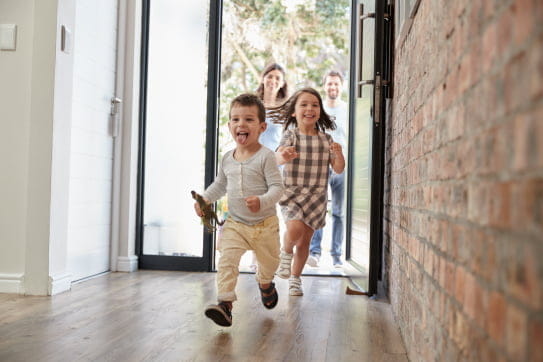 Three children smiling and running through the front door